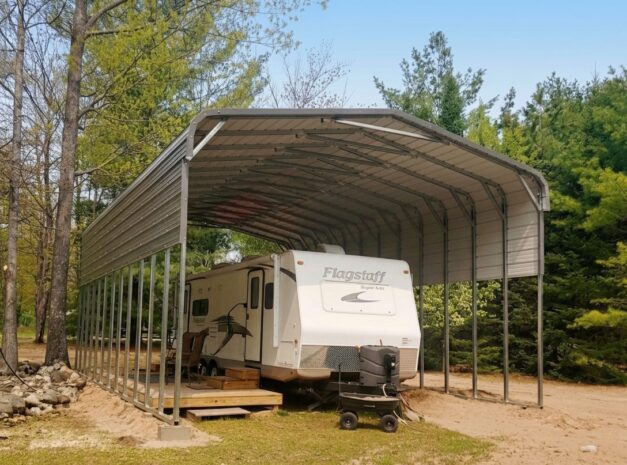 Standard framed carport sheltering a recreational vehicle in a wooded area.