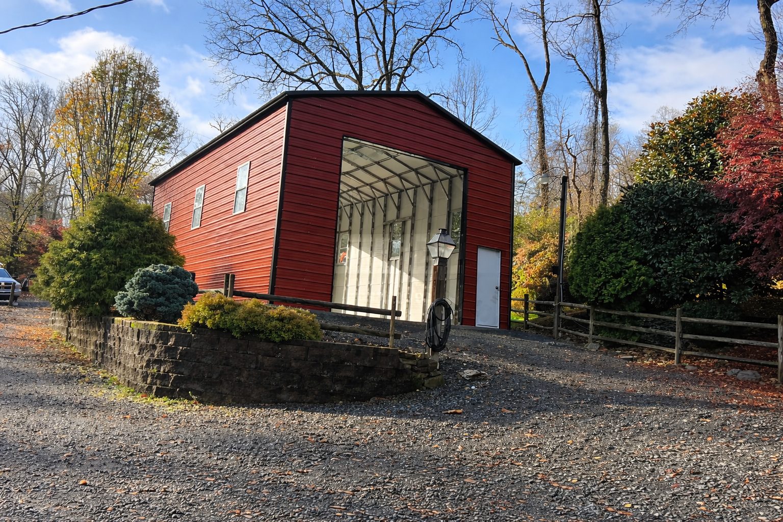 Custom RV carport with a red exterior, set in a scenic landscape with trees and a gravel driveway.