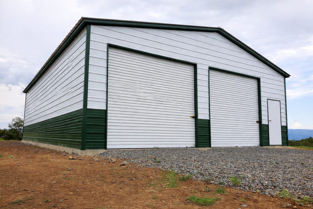 Expansive garage in Cadillac MI with green and white siding, featuring large roll-up doors and a side entrance.