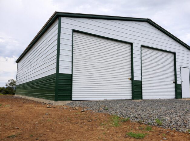 Expansive garage in Cadillac MI with green and white siding, featuring large roll-up doors and a side entrance.