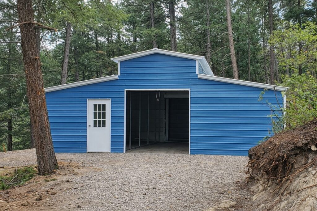 A blue traditional barn with a white door, surrounded by trees and gravel, showcasing available color options.