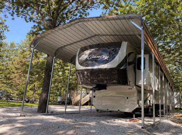 Standard framed carport sheltering an RV in a wooded area, showcasing durable construction and design.