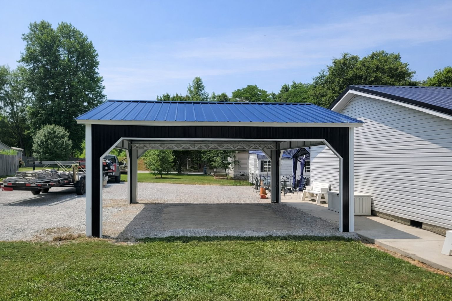 A black and white A-framed carport with a blue metal roof, set in a grassy area near homes in Flint, MI.
