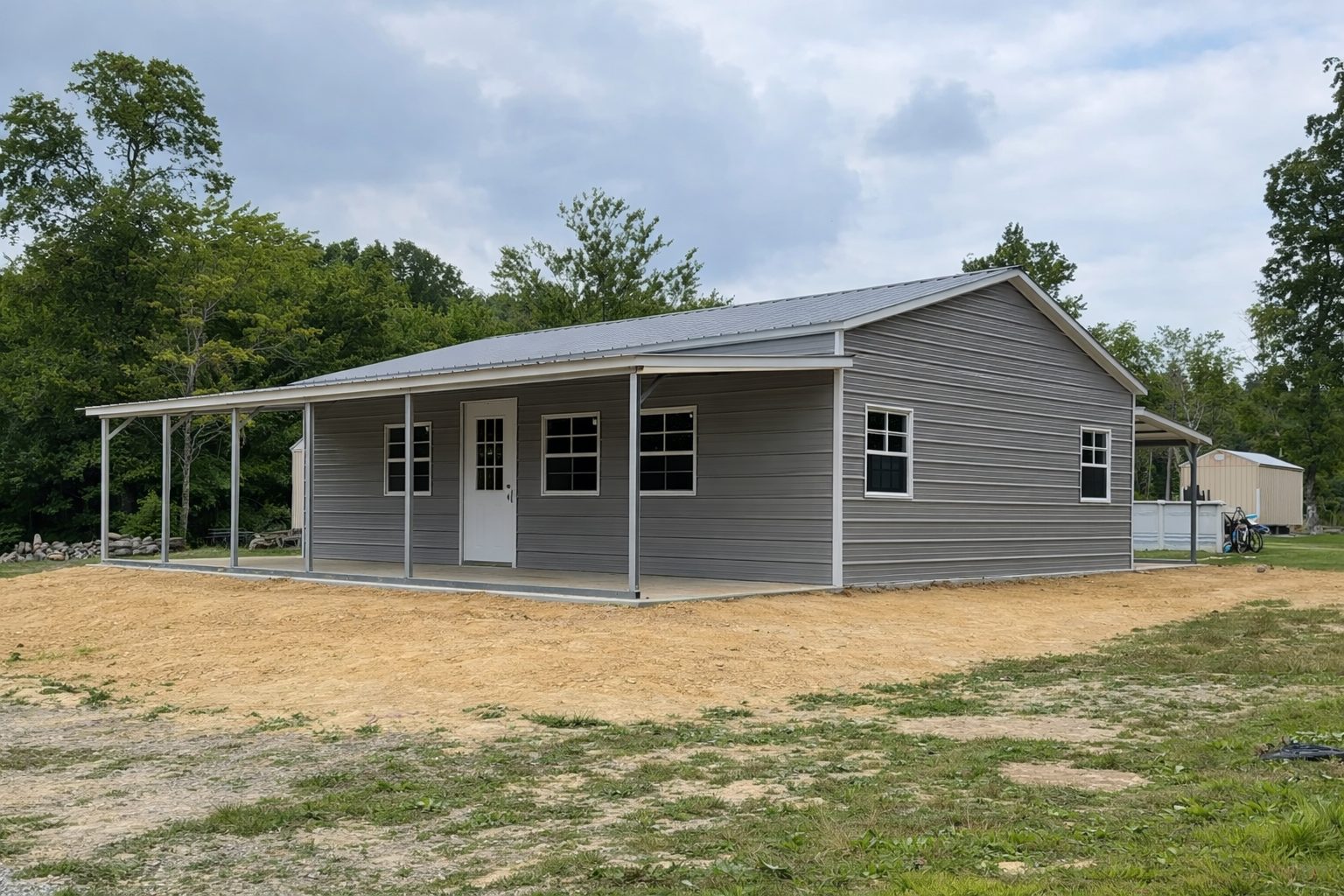 Gray utility shed with a porch, featuring multiple windows, set in a grassy area near trees in Fort Wayne, IN.