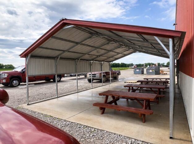 A-frame carport with picnic tables underneath, providing shade and shelter in a parking area.