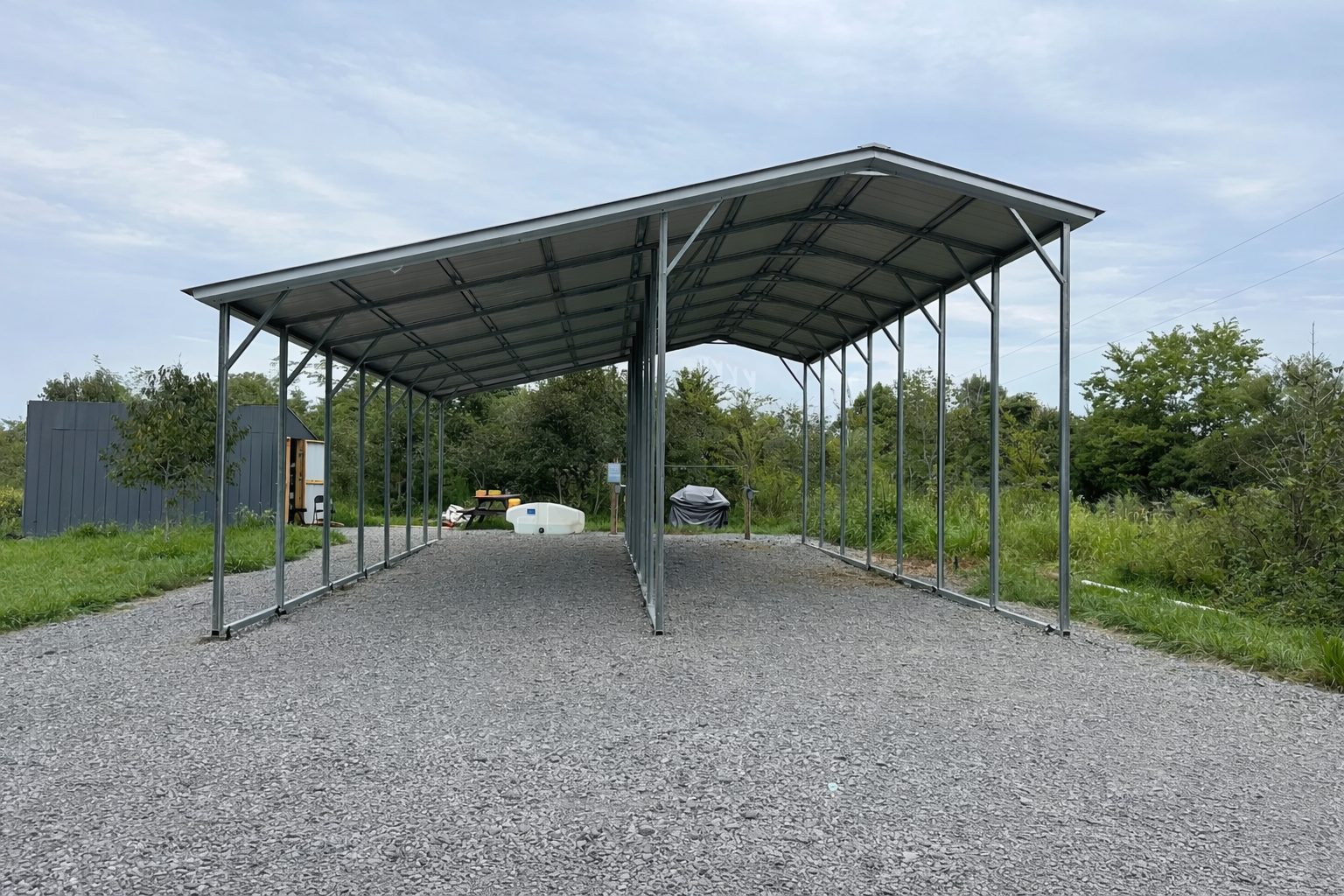 Custom RV carport with a metal frame, set on gravel, surrounded by greenery in Grand Rapids, MI.
