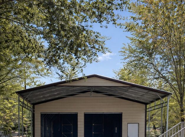 Custom carport in Grayling MI with a spacious design and blue doors, surrounded by trees and gravel driveway.