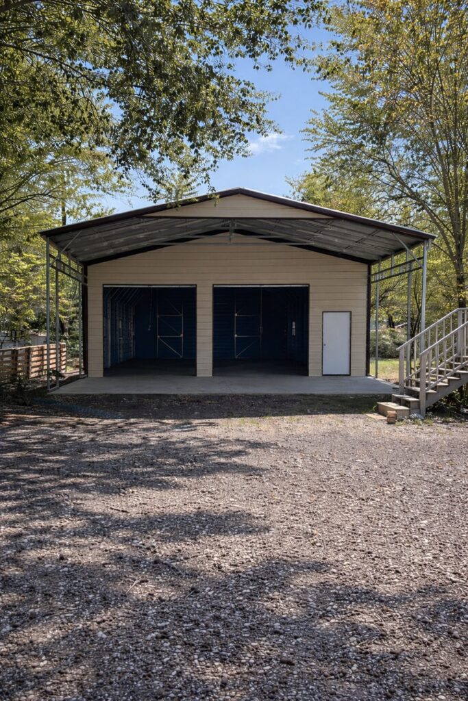 Custom carport in Grayling MI with a spacious design and blue doors, surrounded by trees and gravel driveway.