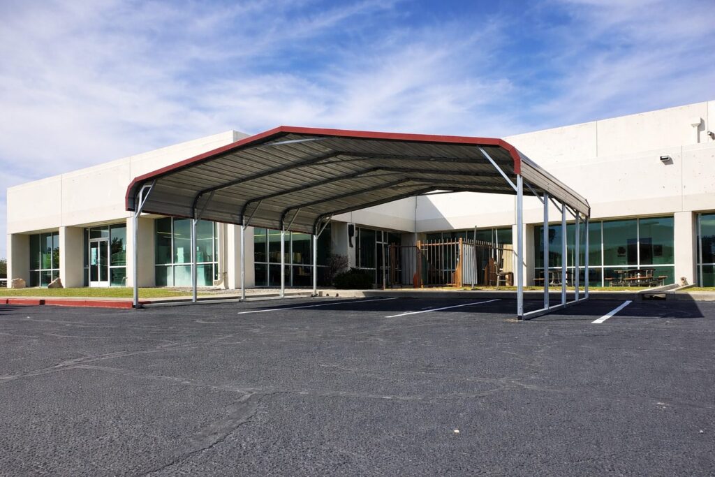 A large steel carport with a red roof, situated in front of a commercial building in Lansing, MI.