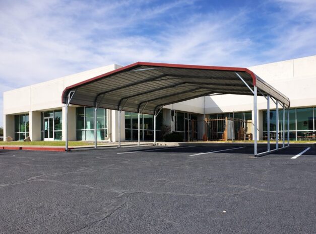 A large steel carport with a red roof, situated in front of a commercial building in Lansing, MI.