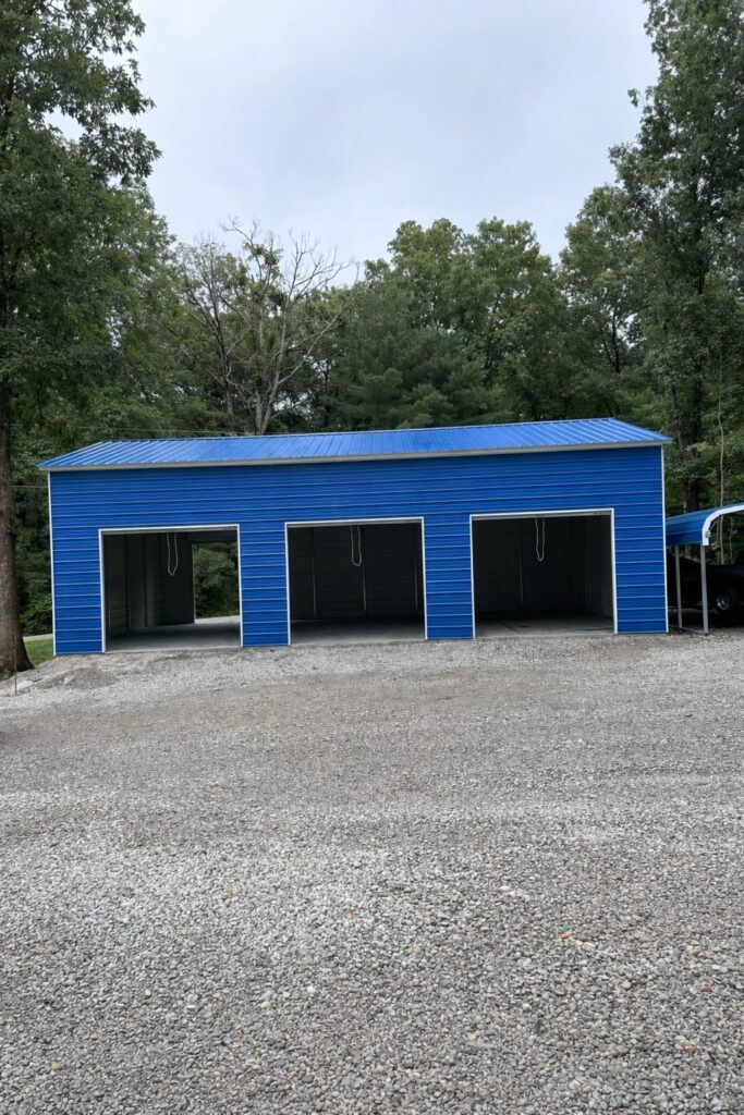 Expansive blue garage with multiple bays, surrounded by trees and gravel driveway, showcasing available color options.