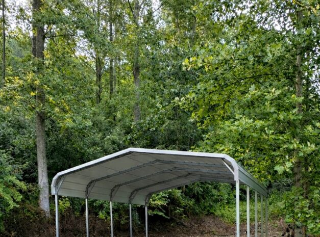 Standard carport in a gravel area surrounded by trees, showcasing durable steel construction.