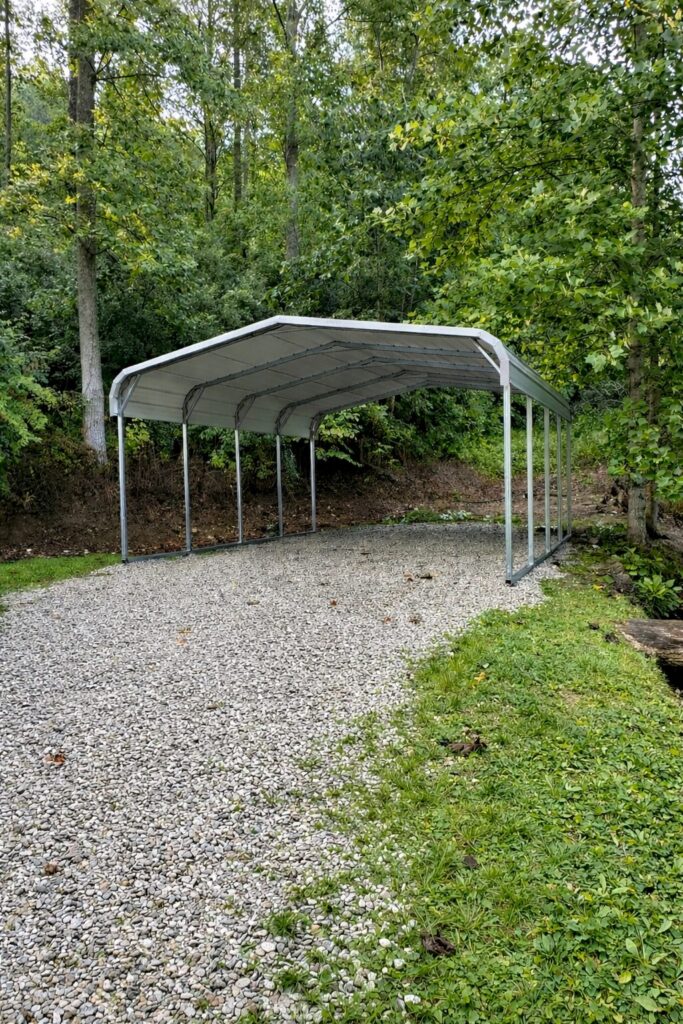 Standard carport in a gravel area surrounded by trees, showcasing durable steel construction.