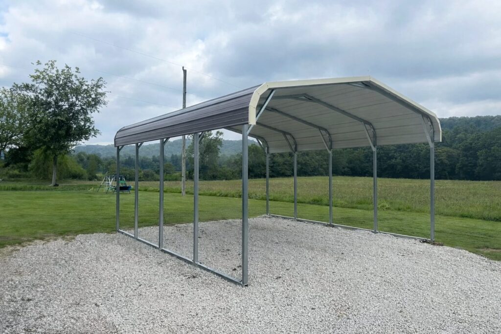 Standard carport with a metal frame and roof, set on gravel in a grassy area near trees.