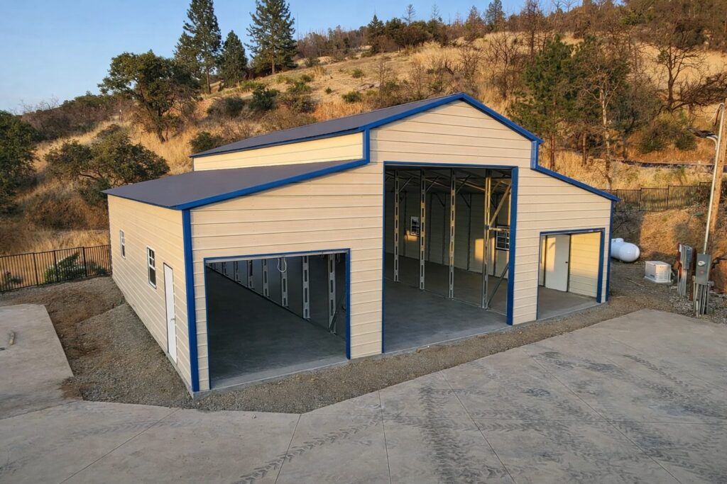 Traditional barn structure with a blue trim, featuring open garage doors, set against a hillside.