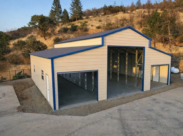Traditional barn structure with a blue trim, featuring open garage doors, set against a hillside.