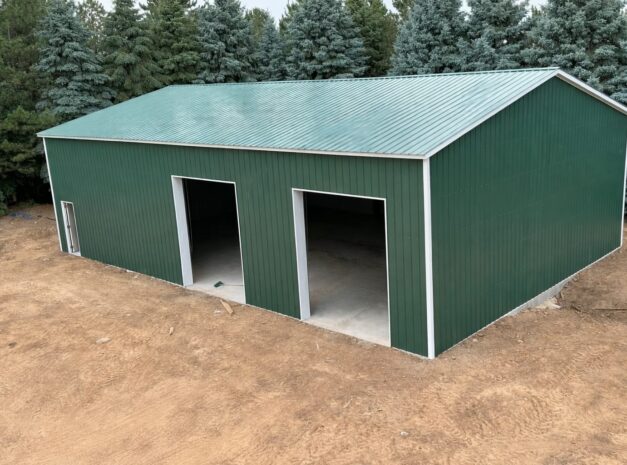 A green steel building with open doors, surrounded by trees, showcasing a Grand Span design in Tarrant County, TX.