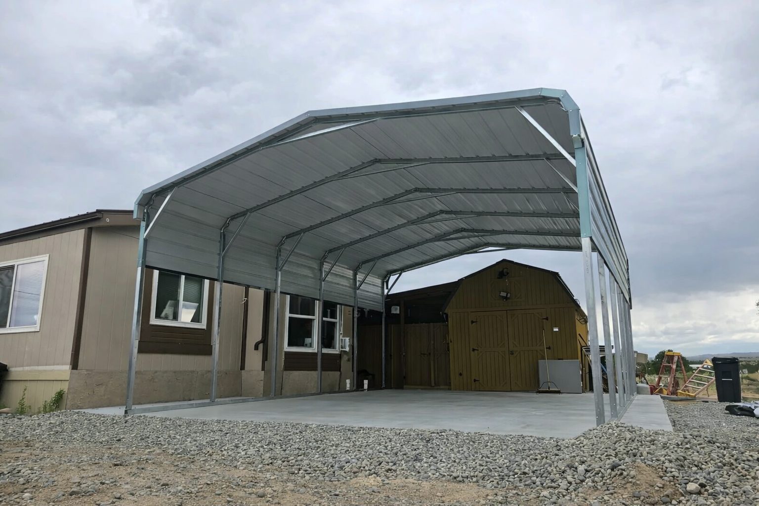 Standard framed carport in Tyler, TX, featuring a metal structure with a concrete base and nearby buildings.